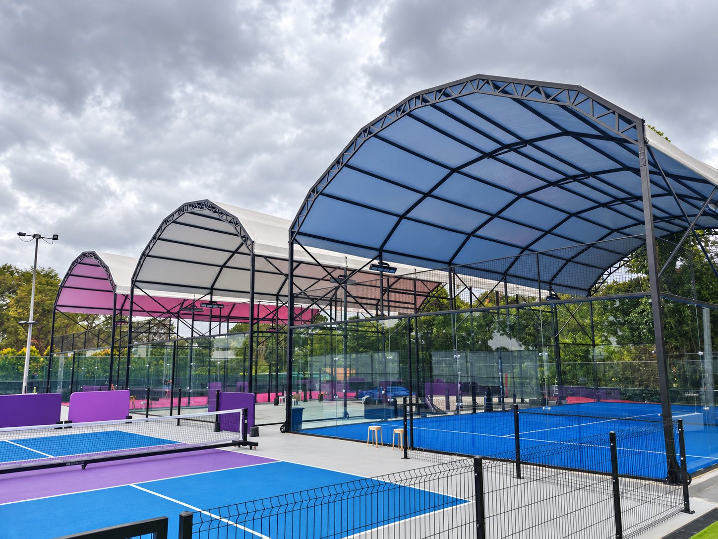 Repeated arched canopies and blue and purple playing surfaces in a mixed racquet-sport venue