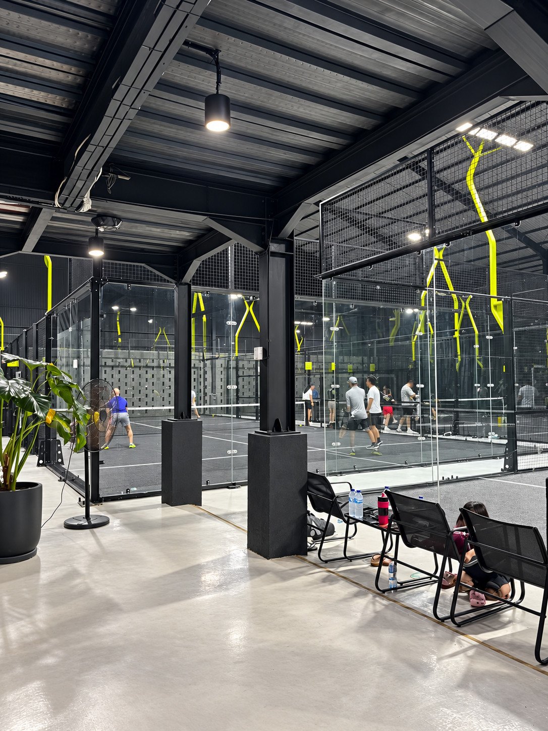 Seating and planting beside glass-enclosed indoor padel courts